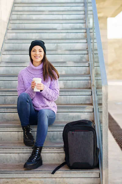 Kvinna i tjugoårsåldern tar en kaffepaus sittandes på några trappsteg på gatan. — Stockfoto