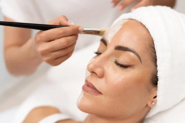 Estética aplicando una máscara a la cara de una mujer de mediana edad en un moderno centro de bienestar. — Foto de Stock