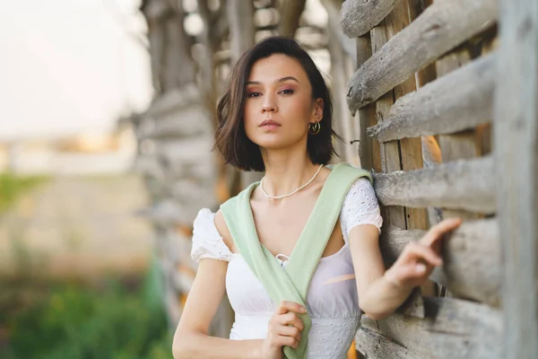 Asiatin posiert in der Nähe einer Tabaktrocknungsanlage, trägt ein weißes Kleid und grüne Gummistiefel. — Stockfoto