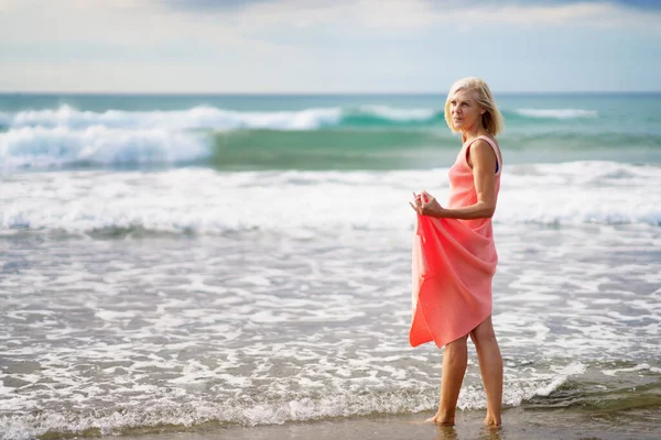 Mature woman enjoying her free time looking at the sea from the shore of the beach. — Stock Photo, Image