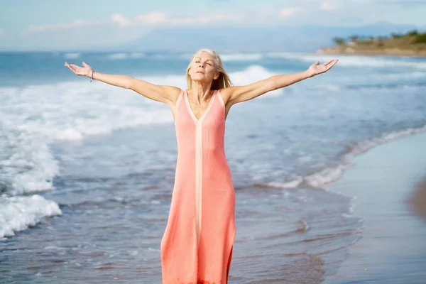 Mooie oudere vrouw spreidt haar armen over een prachtig strand, besteedt haar vrije tijd. — Stockfoto