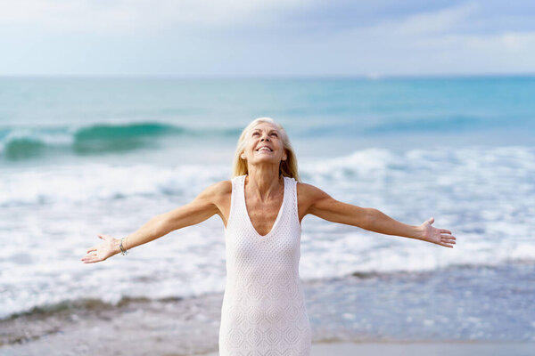 Mature woman opening her arms on the beach, spending her leisure time, enjoying her free time