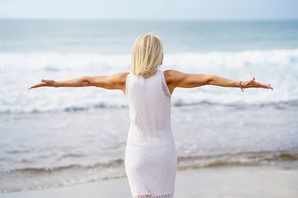 Mature woman opening her arms on the beach, spending her leisure time, enjoying her free time — Zdjęcie stockowe