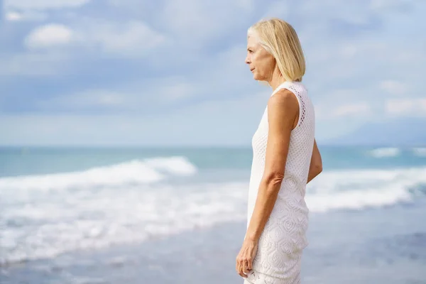 Mature woman gazing serenely at the sea. Elderly female standing at a seaside location — Stock Photo, Image