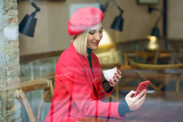 Mujer bebiendo una taza de café en una cafetería, mientras consulta su smartphone. —  Fotos de Stock