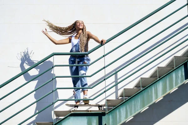 城市楼梯上的黑人女孩，在风中移动着她的彩色辫子。典型的非洲发型. — 图库照片