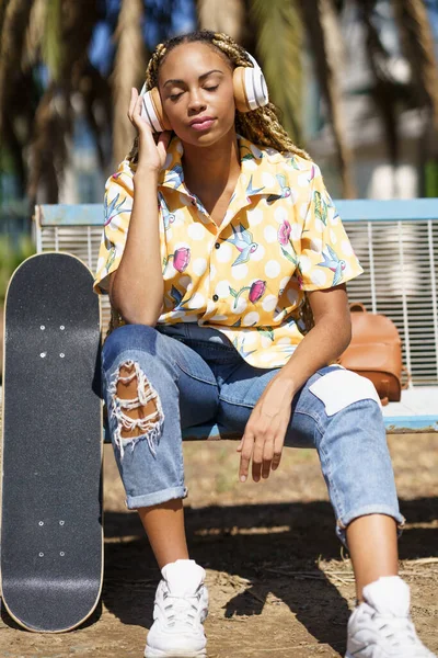 Afrikaanse vrouw met skateboard ontspannen na het rijden skateboard luisteren naar de muziek — Stockfoto