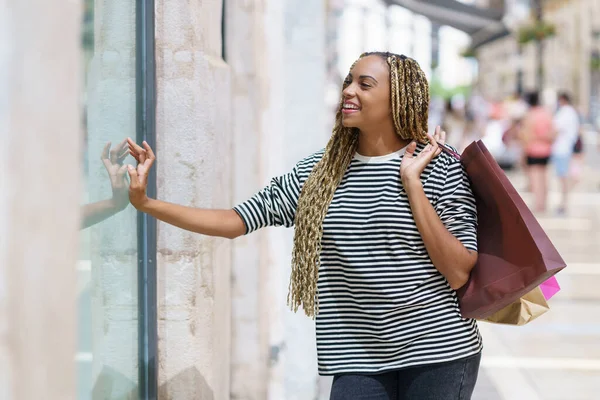 Chica negra frente a un escaparate en una calle comercial. Mujer con trenzas africanas. —  Fotos de Stock