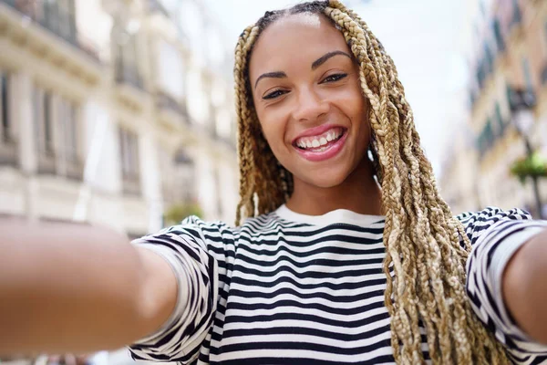 Black girl with afro braids taking a selfie in an urban street with a smartphone. — Stockfoto