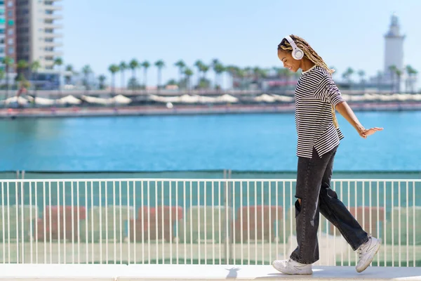 Ung svart flicka balansera medan promenader längs hamnen i en kuststad. — Stockfoto