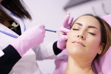 Doktor, yüz gençleştirme tedavisi için bir kadının elmacık kemiklerine hiyalüronik asit enjekte ediyor..