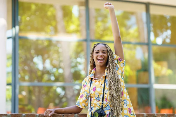 Chica africana con trenzas, levantando el brazo con alegría. Chica sosteniendo una cámara. —  Fotos de Stock