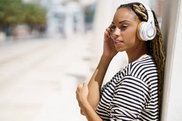 Jonge zwarte vrouw luisteren naar muziek met draadloze hoofdtelefoon buiten. — Stockfoto
