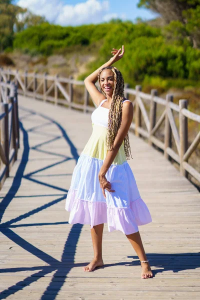 Afrikaanse vrouw draagt een mooie jurk op een promenade op het strand. — Stockfoto