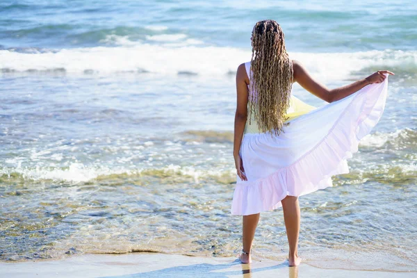 Zwart meisje wandelend langs de kust van het strand in een prachtige lange jurk. — Stockfoto