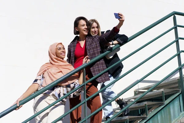 Glada multiracial flickvänner som tar selfie på smartphone på trappor — Stockfoto