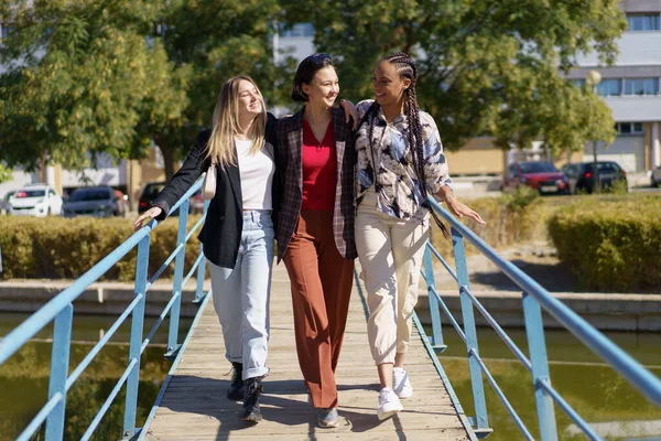 Leende olika vänner kramas när du promenerar på smal gångbro — Stockfoto