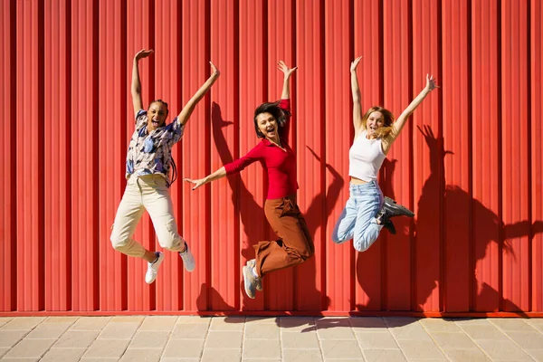 Lekfulla unga mångsidiga vänner hoppar på gatan mot röd vägg — Stockfoto
