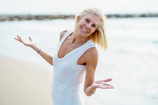 Улыбающаяся зрелая женщина, гуляющая по пляжу, проводящая досуг, наслаждаясь свободным временем — стоковое фото