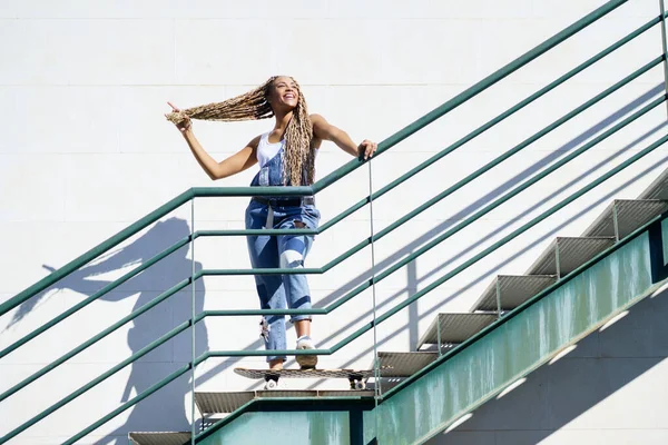 Ragazza nera su una scala urbana, tenendo le trecce colorate. Tipica acconciatura africana. — Foto Stock