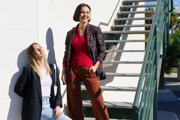 Encantadas mujeres jóvenes sonriendo mientras descansan cerca de las escaleras en el parque —  Fotos de Stock