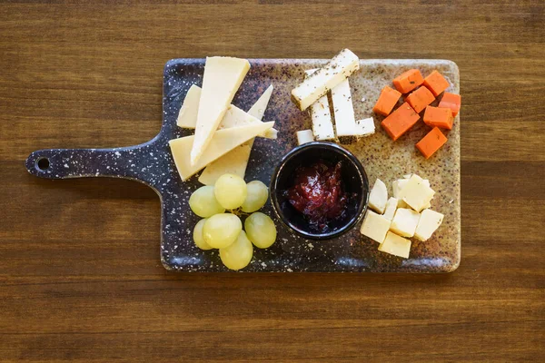 Cheese and grapes with sauce on charcuterie board — Stock Photo, Image