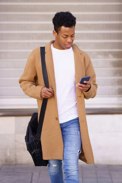 Mladý černoch se dívá na svůj smartphone při chůzi po ulici. — Stock fotografie