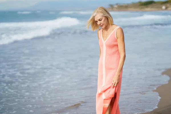 Volwassen vrouw aan de kust van een strand. Oudere vrouw geniet van haar pensioen op een terugtocht aan zee. — Stockfoto