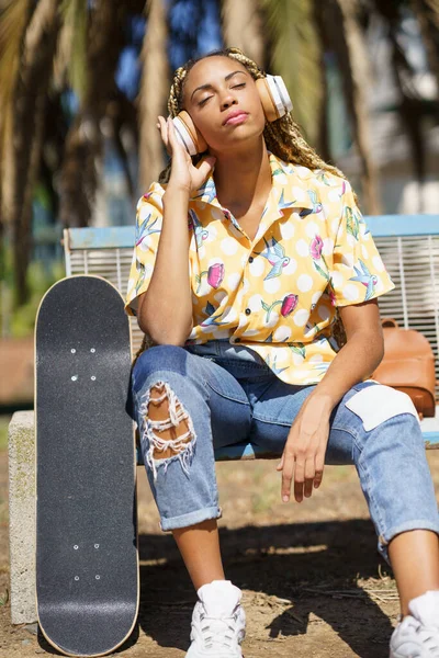 Afrikaans meisje met skateboard ontspannen na paardrijden skateboard luisteren naar de muziek — Stockfoto