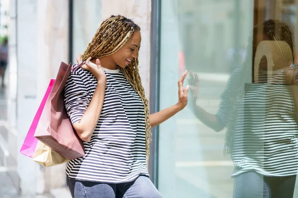 Mulher negra na frente de uma vitrine em uma rua comercial. Mulher com tranças africanas. — Fotografia de Stock
