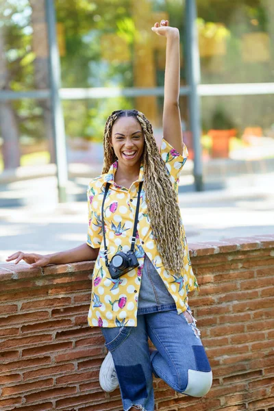 Черная женщина с африканскими косичками, поднимает руку от радости. Девушка с камерой. — стоковое фото