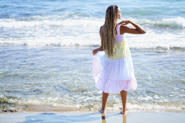 Mulher negra andando ao longo da costa da praia vestindo um belo vestido longo. — Fotografia de Stock