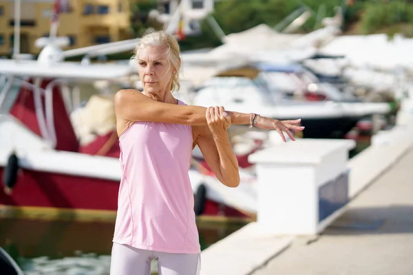 Fit oudere sportvrouw stretching armen in de haven — Stockfoto