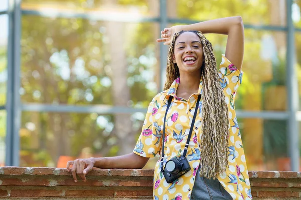Zwarte vrouw met Afrikaanse vlechten, die haar arm optilt van vreugde. Meisje met een camera. — Stockfoto