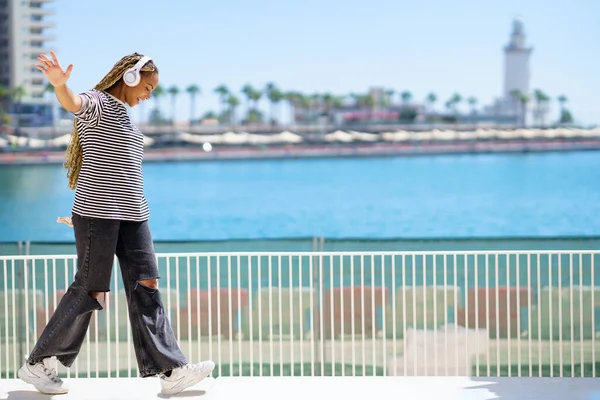 Young black girl balancing while strolling along the harbor of a coastal city. — Stockfoto