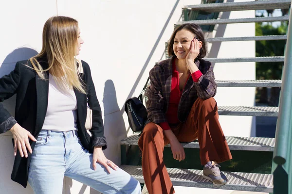 Encantadas mujeres jóvenes sonriendo mientras descansan cerca de las escaleras en el parque —  Fotos de Stock