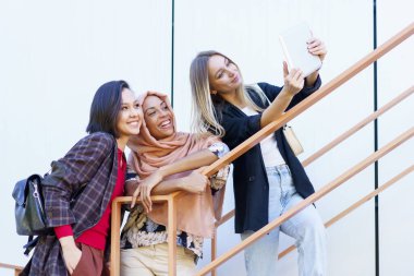 Heyecanlı genç çok ırklı kadın milenyumlar gülümsüyor ve tabletten selfie çekiyor.