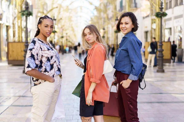 Çok ırklı kadın arkadaşlar ellerinde alışverişlerle caddede dikiliyorlar. — Stok fotoğraf