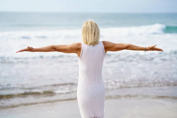 Anonieme volwassen vrouw met uitgestrekte armen aan de kust — Stockfoto