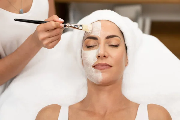 Estetica applicare una maschera al viso di una donna di mezza età nel moderno centro benessere. — Foto Stock