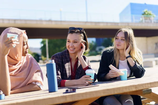 Sonriendo diversas mujeres jóvenes tomando un café y charlando en el parque de la ciudad —  Fotos de Stock