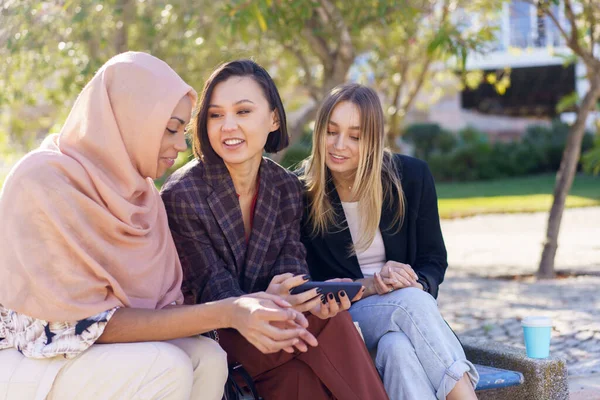 Sorridente giovani ragazze diverse guardare video su smartphone nel parco — Foto Stock