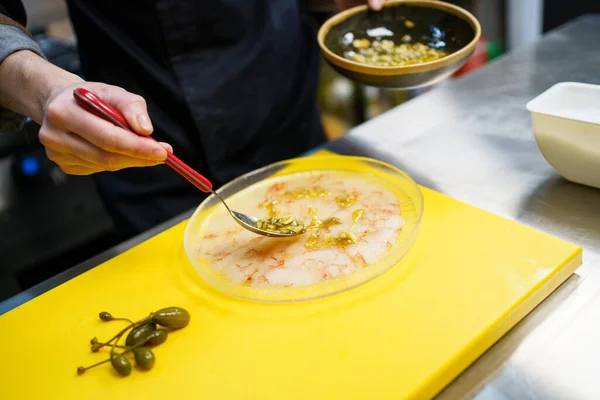 Cozinheiro anônimo espalhando molho de noz de pinheiro em um prato de carpaccio de camarão — Fotografia de Stock