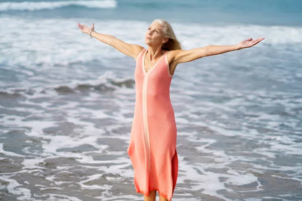 Mulher madura bonita abrindo os braços em uma bela praia, desfrutando de seu tempo livre — Fotografia de Stock