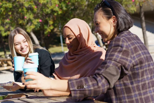 Feliz multiétnicas jóvenes tomando café para llevar y sonriendo en el parque — Foto de Stock