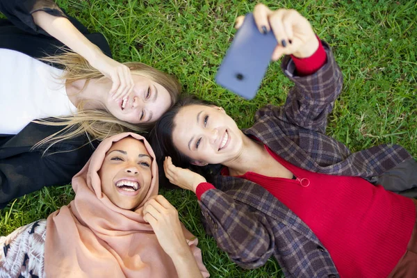 Wesoły różnorodne przyjaciele biorąc selfie na smartfonie na trawie — Zdjęcie stockowe