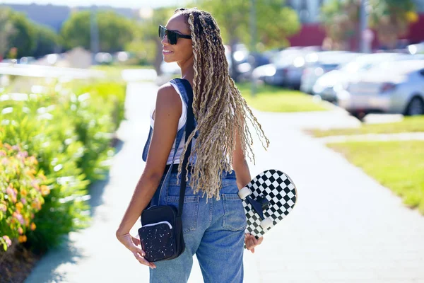 Svart kvinna med skateboard promenader i staden — Stockfoto