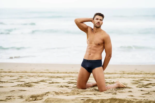 Przystojny mężczyzna na kolanach na piasku plaży. — Zdjęcie stockowe