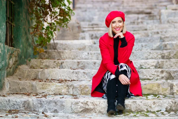 Naisellinen tyylikäs nainen lepää kaupungin portailla ja hymyilee — kuvapankkivalokuva