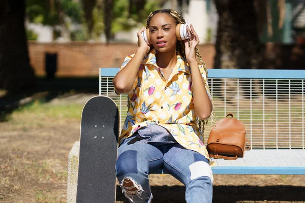 African girl with skateboard relaxing after riding skateboard listening to the music — Stock Photo, Image
